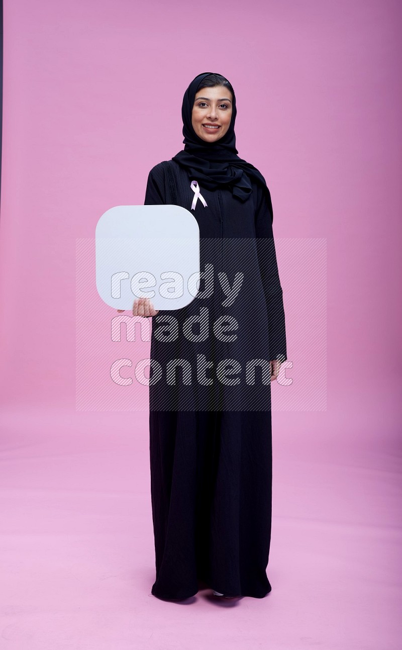 Saudi woman wearing pink ribbon on Abaya standing holding social media signs on pink background