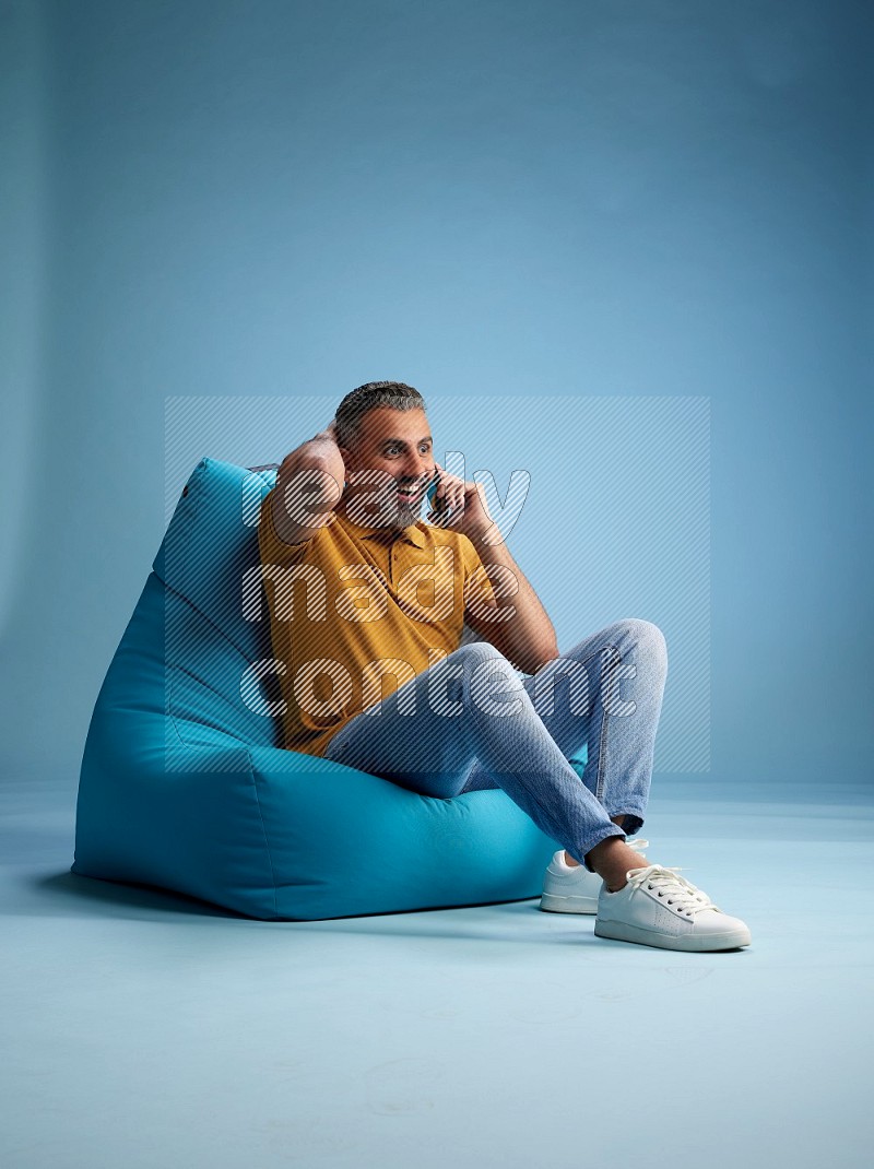 A man sitting on a blue beanbag and talking on the phone