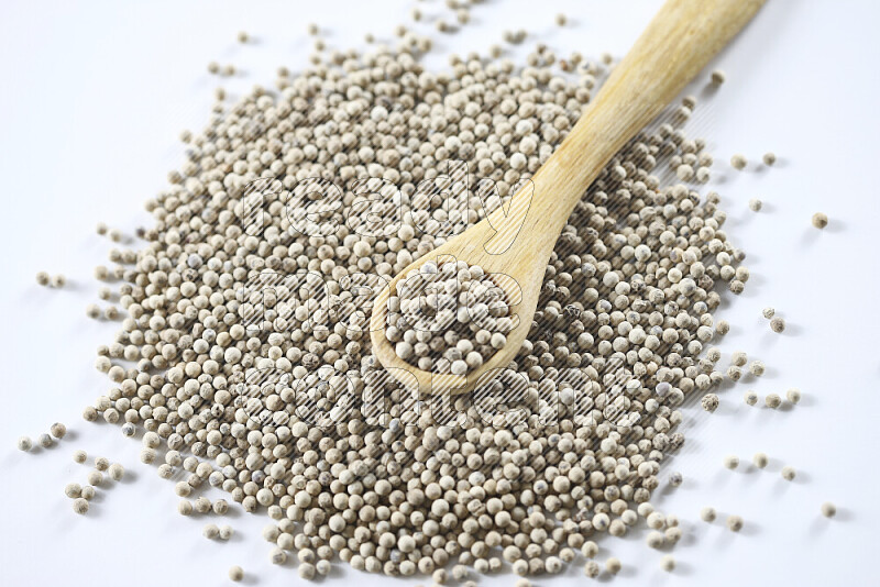 White pepper beads with wooden spoon on white background