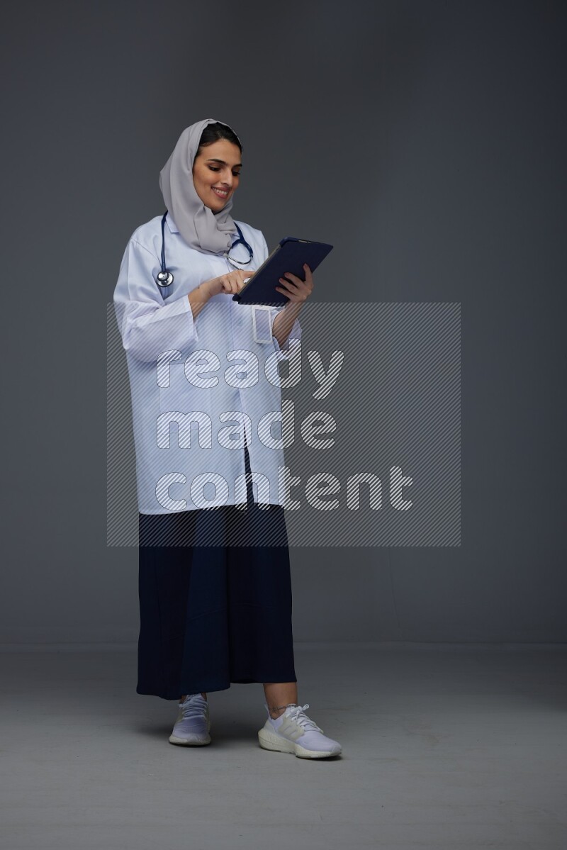 A Saudi doctor wearing a light gray head scarf standing and crossing her hands eye level on a grey background