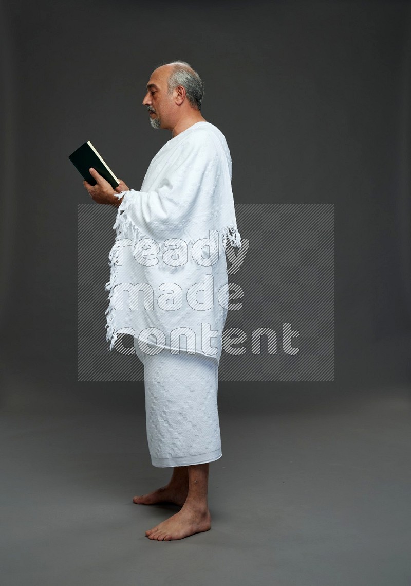 A man wearing Ehram Standing reading quran on gray background