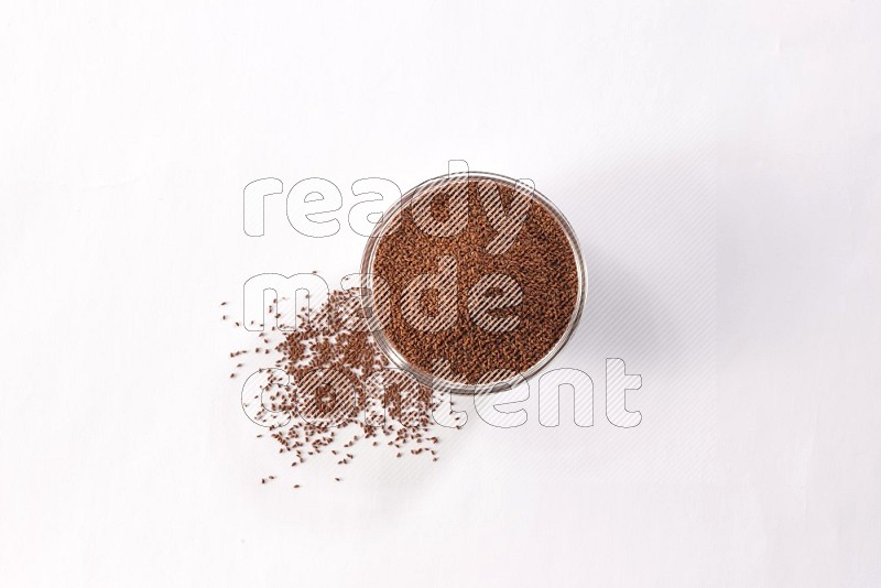 A glass bowl full of garden cress seeds with more seeds spread on a white flooring