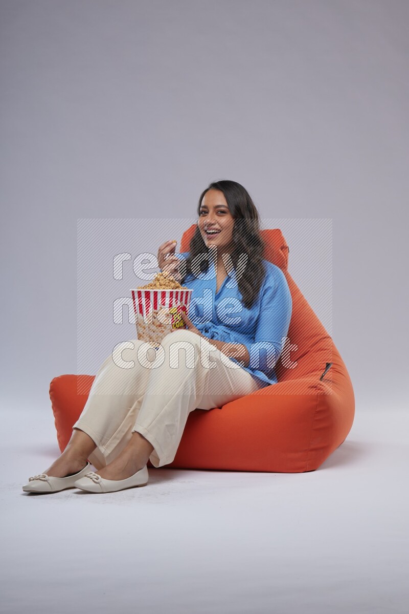 A woman sitting on an orange beanbag and eating popcorn