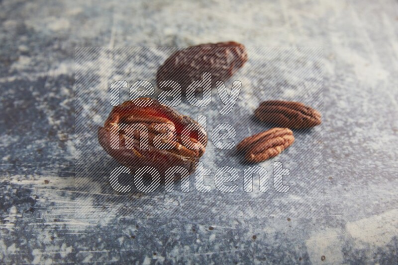 two pecan stuffed madjoul dates on a rustic blue background