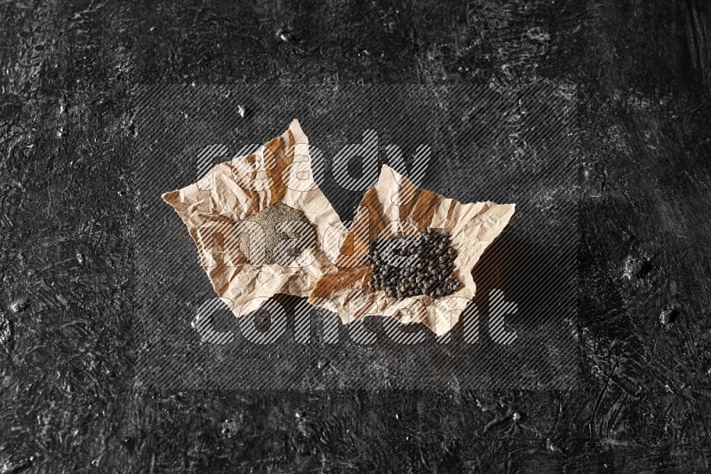 حبوب وبودرة الفلفل الأسود في قطع من الورق علي خلفية سوداء