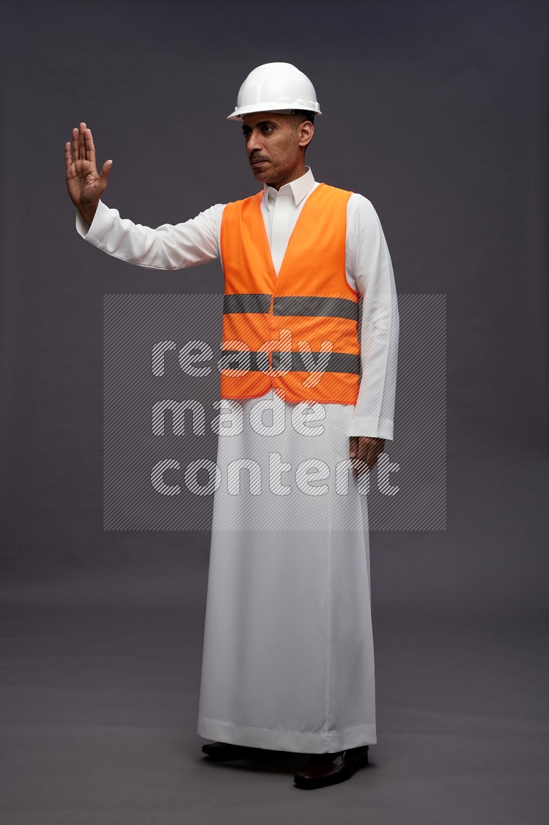 Saudi man wearing thob with engineer vest standing interacting with the camera on gray background