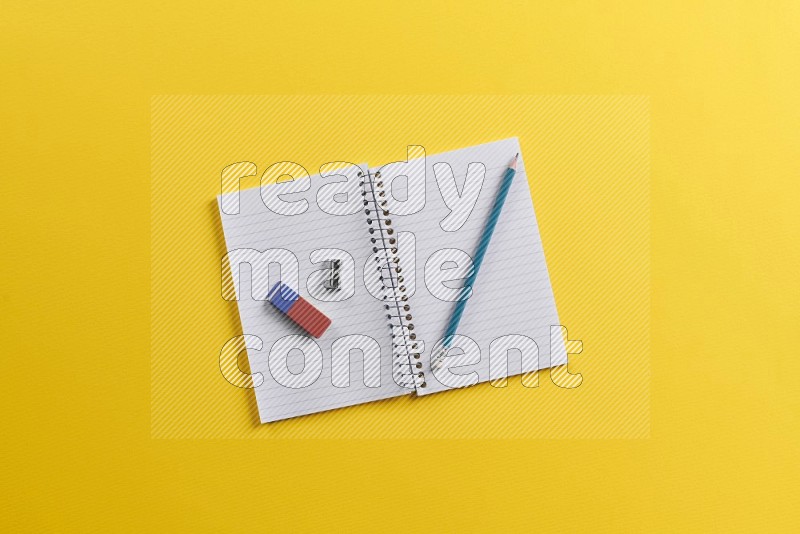 A blank open notebook with school supplies on yellow background (Back to school)