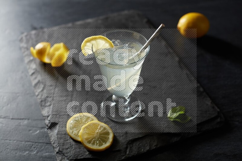 A glass of lemon juice with a straw on black background