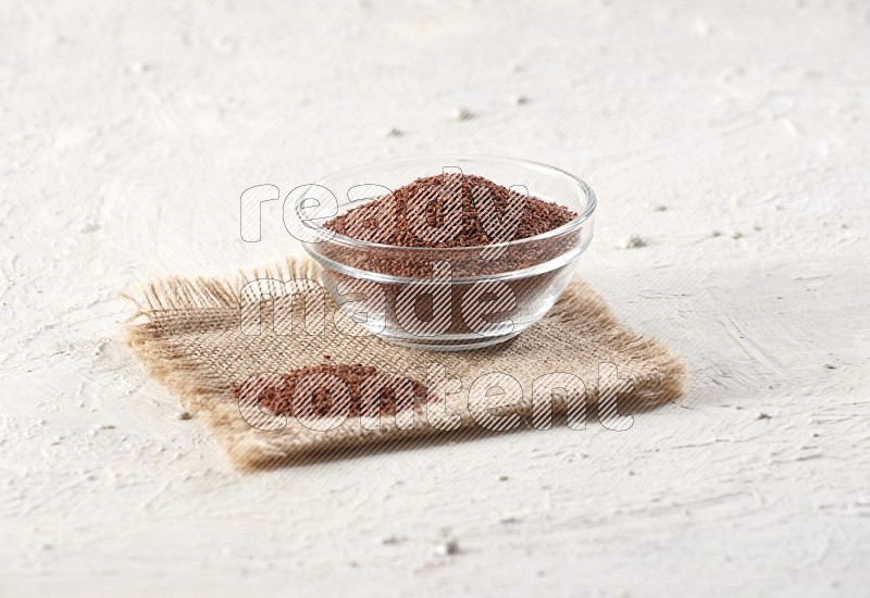 A glass bowl full of garden cress seeds on a burlap fabric on textured white flooring