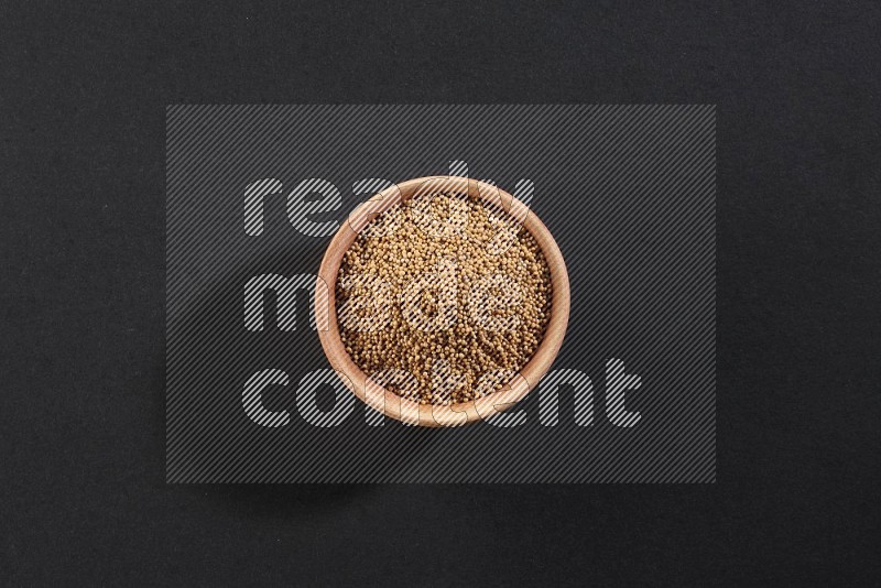 A wooden bowl full of mustard seeds on a black flooring