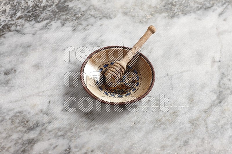 Decorative Pottery Plate with wooden honey handle in it, on grey marble flooring, 65 degree angle