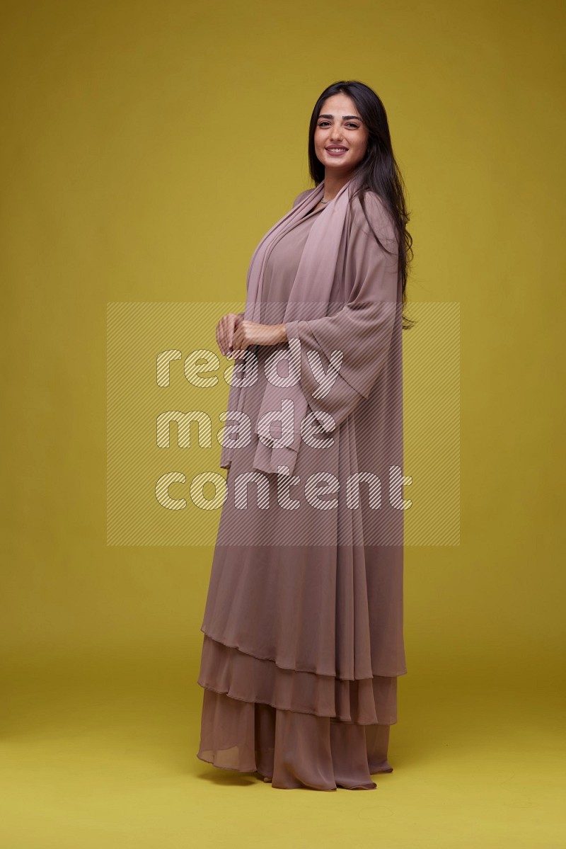 A woman Posing on a Yellow Background wearing Brown Abaya