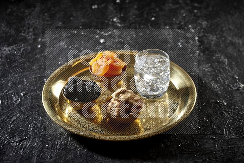 فواكه مجففة في أطباق معدنية مع الماء على صينية علي خلفية سوداء