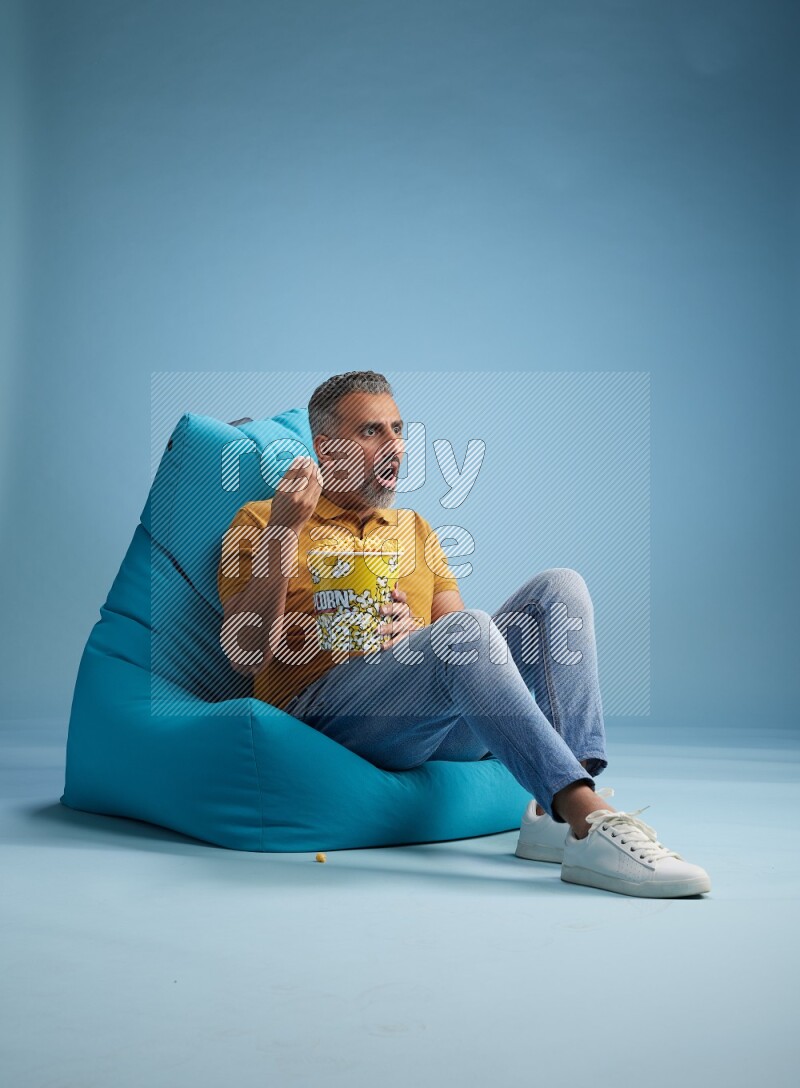 A man sitting on a blue beanbag and eating popcorn
