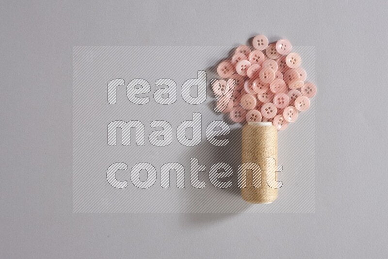 A beige sewing thread spool with colored buttons on grey background