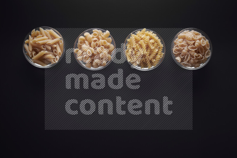 Different pasta types in glass bowls on black background