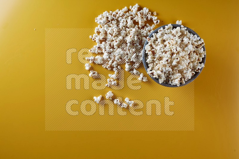 A multicolored pottery bowl full of popcorn with popcorn beside it on a yellow background in different angles