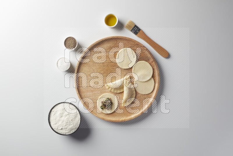 two closed sambosas and one open sambosa filled with meat while flour, salt, black pepper and oil with oil brush aside in a wooden dish on a white background