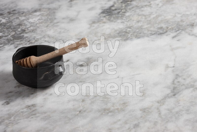 Black pottery bowl with wooden honey dipper in it on grey marble background