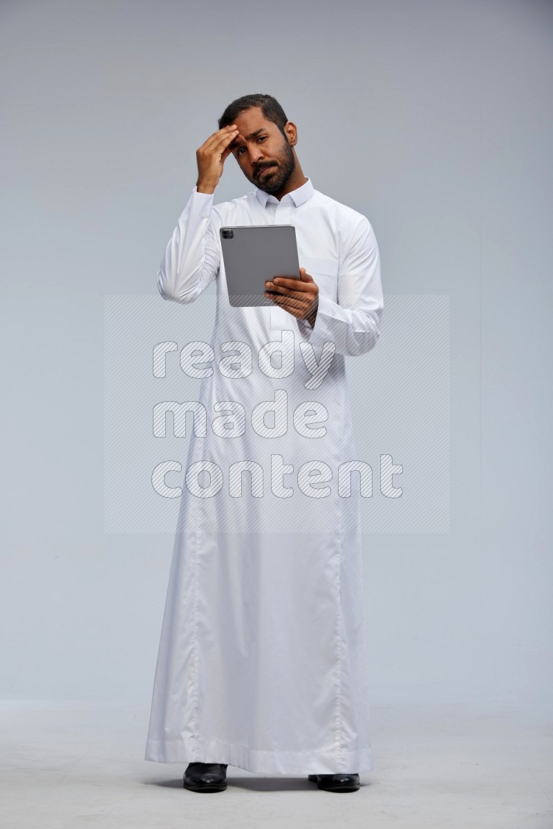 Saudi man wearing Thob standing working on tablet on Gray background