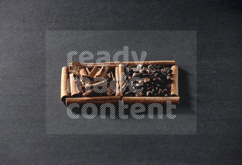 مربعان من أعواد القرفة ممتلئان بحبوب القهوة وقطع من القرفة علي خلفية سوداء