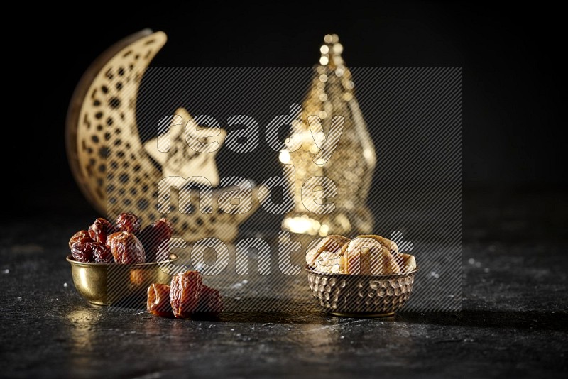 Dates in a metal bowl with dried figs beside golden lanterns in a dark setup