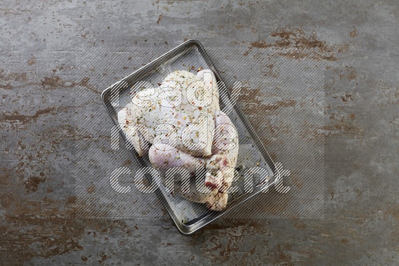 whole Raw chicken on a small oven trey direct on a rustic grey background