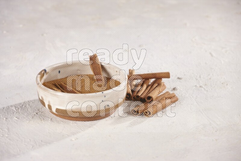 Ceramic bowl full of cinnamon powder with cinnamon sticks on the side on white background