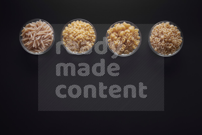 Different pasta types in glass bowls on black background