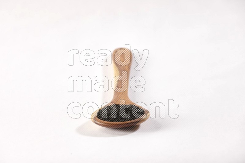 A wooden ladle full of black seeds on a white flooring