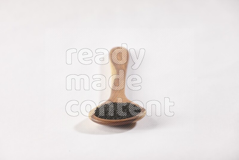 ملعقة خشبية كبيرة ممتلئة ببذور حبة البركة علي خلفية بيضاء