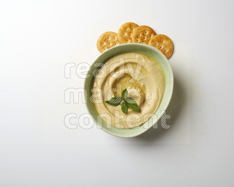 Hummus in a green plate garnished with mint on a white background