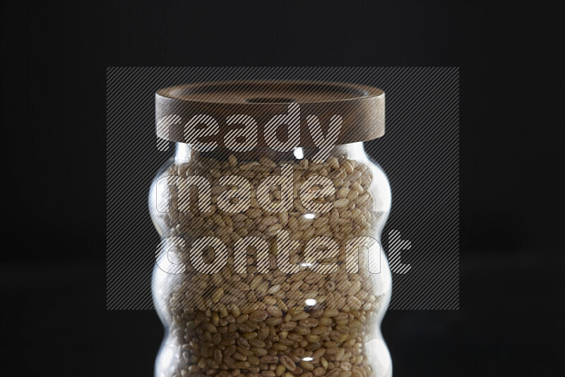Hulled wheat in a glass jar on black background