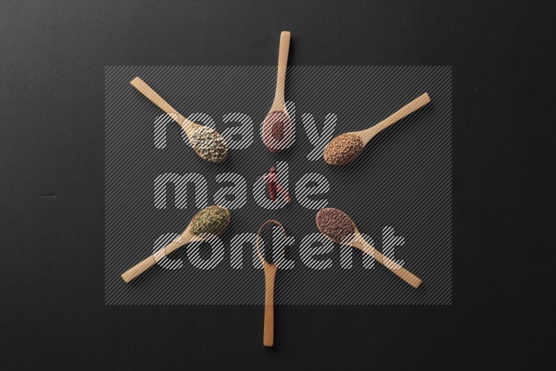 wooden spoons filled with white peppers, mustard seeds, black seeds, garden cress, cumin and flax on black flooring and shaped like a clock