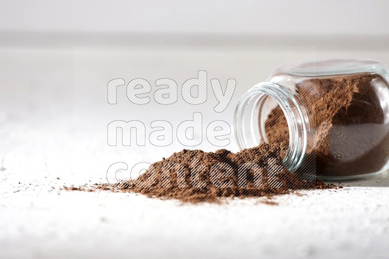 A flipped glass spice jar full of cloves powder and powder came out of it on textured white flooring