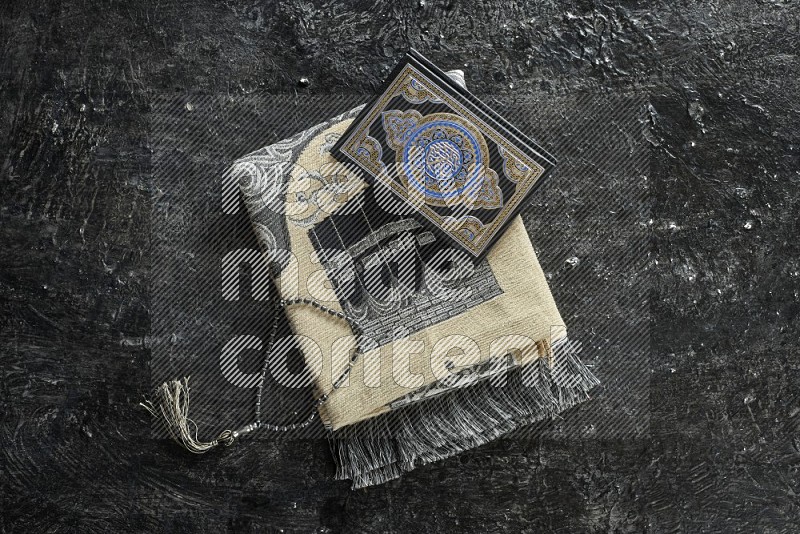 A prayer rug with different elements such as quran and prayer beads on black textured background