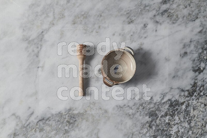 Multicolored pottery bowl with wooden honey dipper on the side on grey marble background