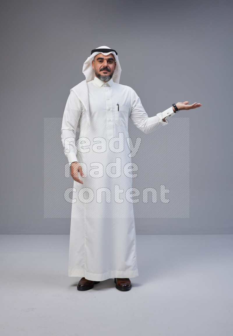 Saudi man Wearing Thob and white Shomag standing interacting with the camera on Gray background