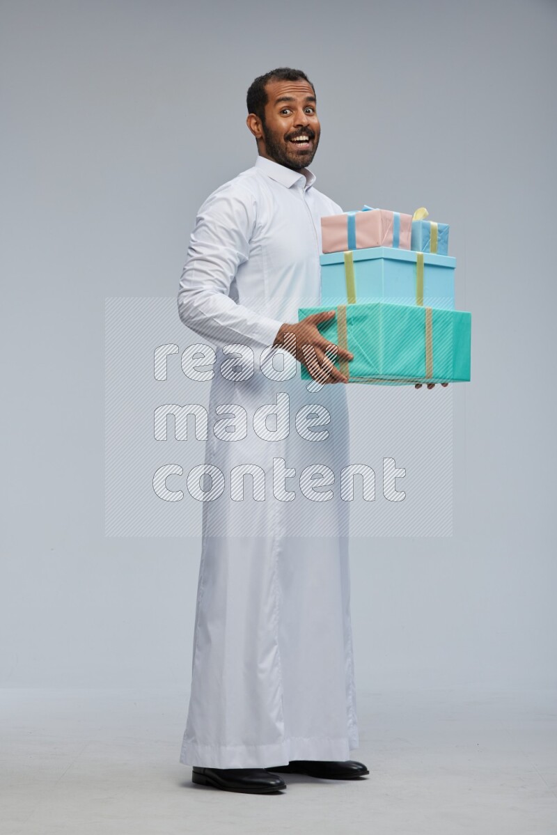 Saudi man Wearing thob standing holding gift box on Gray background