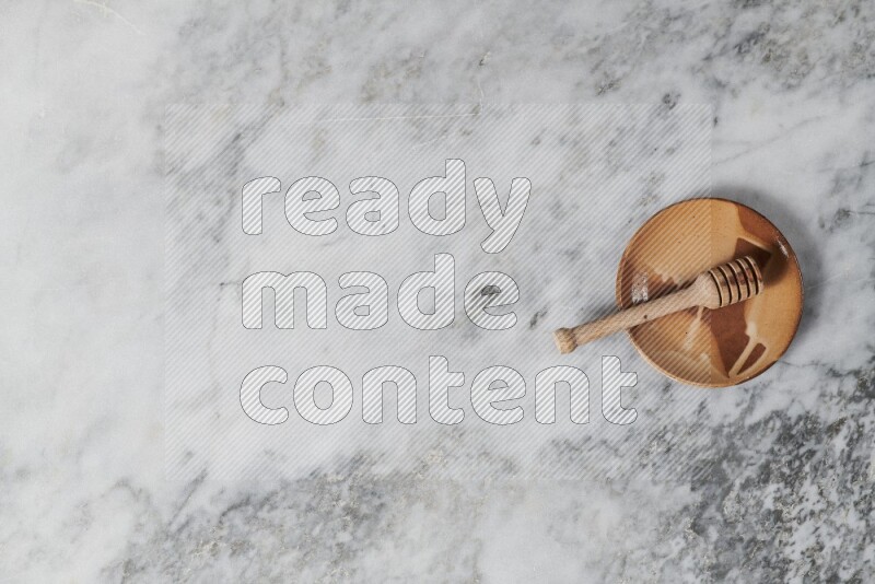 Multicolored pottery plate with wooden honey dipper in it on grey marble background