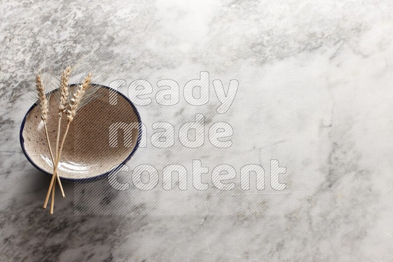 Wheat stalks on multicolored pottery bowl on grey marble background
