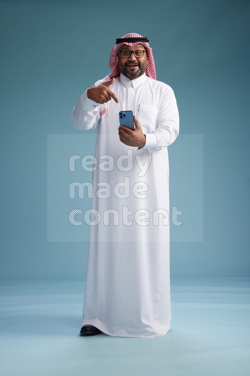Saudi Man with shimag Standing texting on phone on blue background