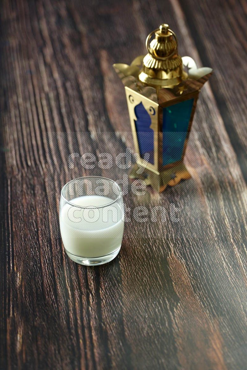 A golden lantern with different drinks, dates, nuts, prayer beads and quran on brown wooden background