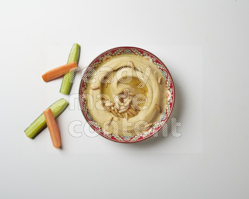 Hummus in a red plate with patterns garnished with pine nuts on a white background