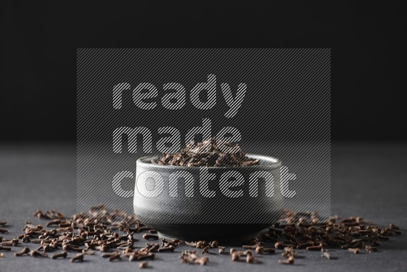 A black pottery bowl full of cloves on a black flooring