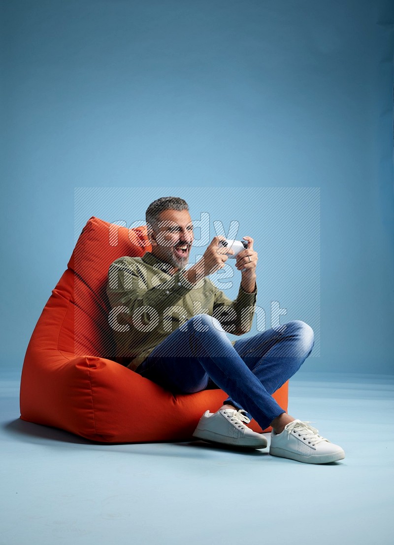 A man sitting on an orange beanbag and gaming with joystick