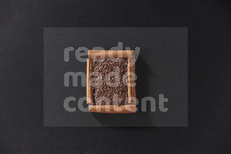 A single square of cinnamon sticks full of flaxseeds on black flooring