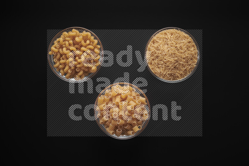 Different pasta types in glass bowls on black background