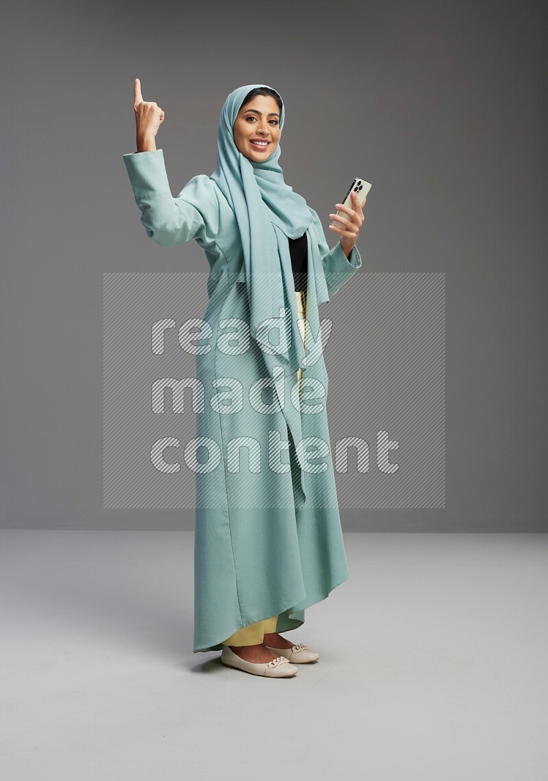 Saudi Woman wearing Abaya standing texting on phone on Gray background