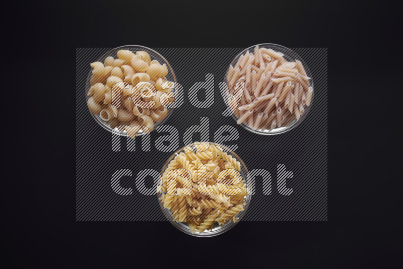 Different pasta types in glass bowls on black background
